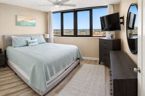 Camera da letto con un letto, una TV, una cassettiera e vista sulla città.