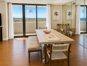 A dining area with a wooden table, cushioned chairs, and a view of the ocean through large glass doors.
