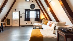 A cozy attic bedroom with a sloped ceiling, a bed with a yellow throw, a lamp, and a small table.
