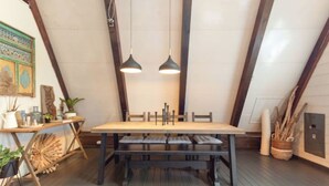 A dining area with a wooden table and benches, two pendant lights, and a rustic decor with plants and wooden elements.