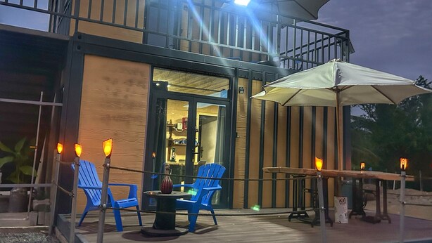 Un bâtiment moderne doté d’un balcon et d’un espace extérieur aménagé avec des chaises bleues et une table.