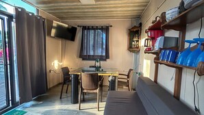 Un espace de vie compact doté d’un plafond en bois, d’une table à manger avec des chaises, d’un canapé et d’une étagère murale où sont rangés de la vaisselle.