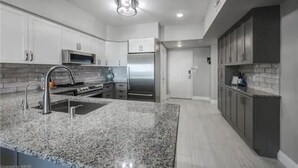Una cocina moderna con encimeras de granito, electrodomésticos de acero inoxidable y armarios blancos.