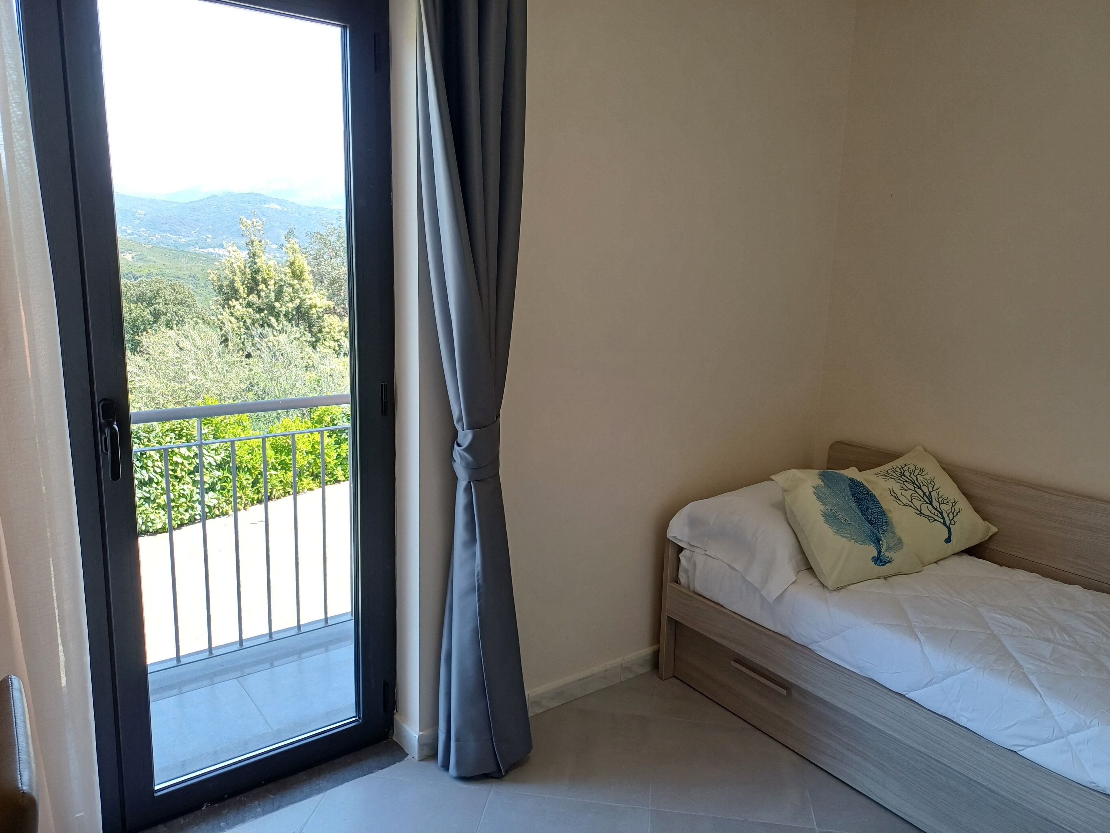 A bedroom with a bed, a window with curtains, and a view of greenery.