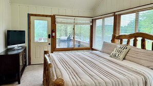 Une chambre à coucher avec un lit, un téléviseur posé sur une commode et une porte donnant sur une terrasse extérieure.