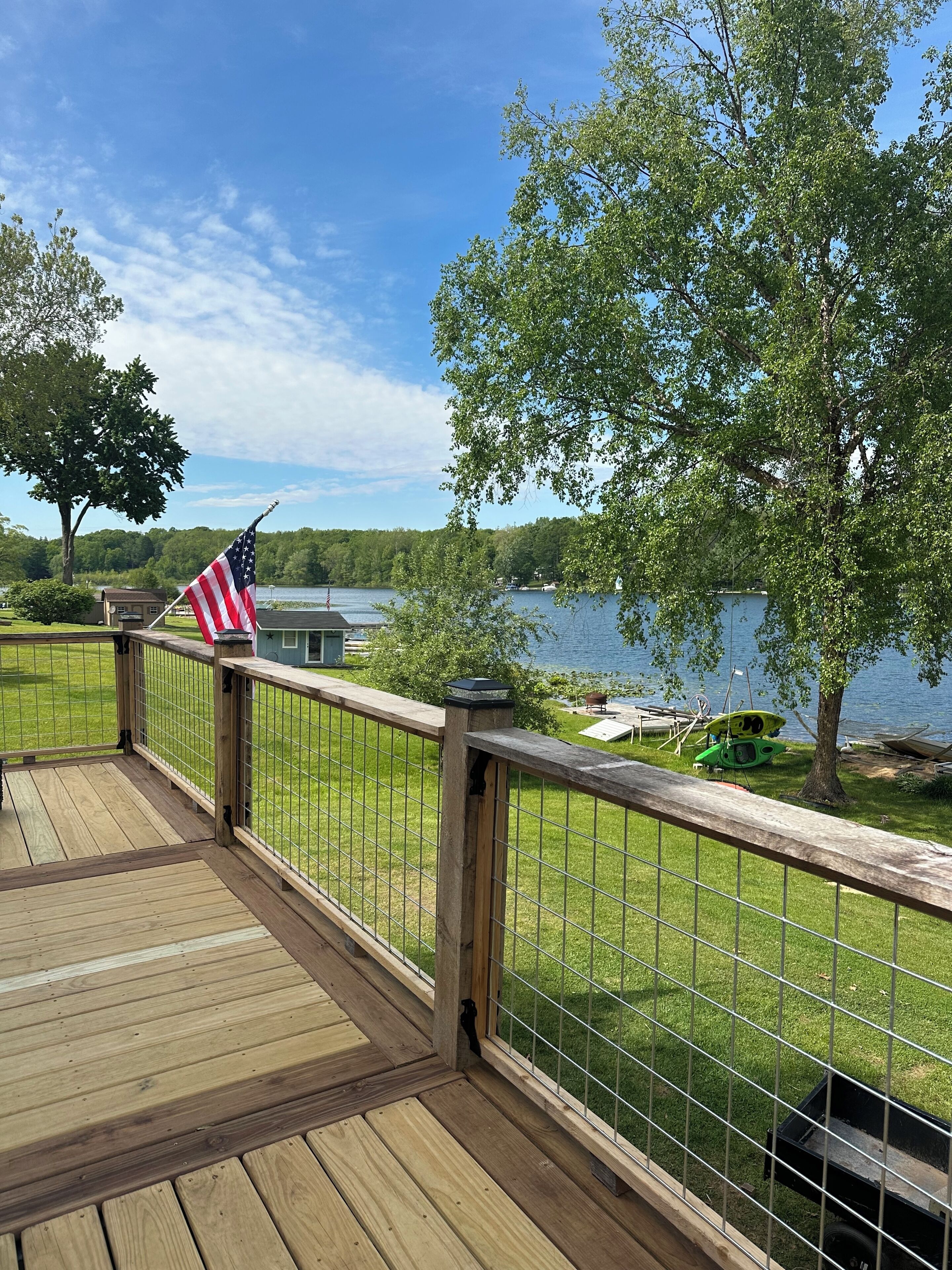 En træterrasse med gelænder i metal, udsigt over en sø, et amerikansk flag og en bådebøje.