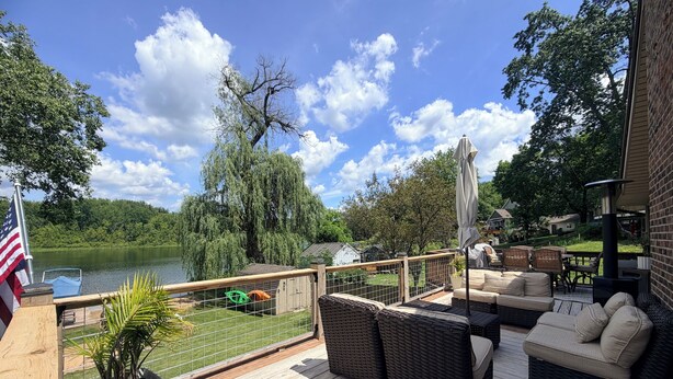 Une terrasse dotée de meubles en osier, offrant une vue sur un lac, et ornée d’un drapeau.