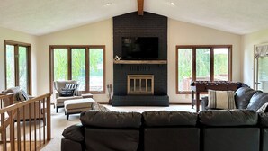 Un salon spacieux doté d’une cheminée, de grandes fenêtres et d’un ventilateur de plafond.