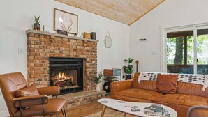 A living room with a brick fireplace, leather furniture, and a view through a large window.