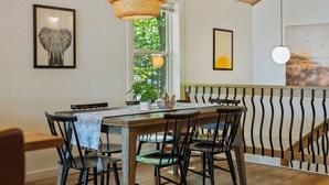 A dining area with a wooden table, black chairs, a woven pendant light, and framed artwork on the walls.