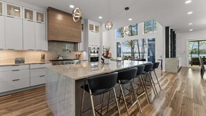Une cuisine moderne dotée d’un grand îlot central, de tabourets de bar et offrant une vue sur l’extérieur.
