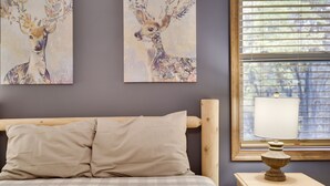 Un dormitorio con cama, dos cuadros de ciervos en la pared, una mesita de noche con lámpara y una ventana con persianas.