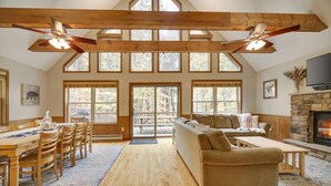 Un salón espacioso con techo de madera, ventanas amplias, chimenea de piedra y una zona de estar acogedora.