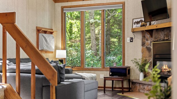 A cozy living room with a grey sofa, wooden staircase, and a stone fireplace. - Harmony Ridge by AvantStay | Fireplace, Large Deck & Forest Views (Lake Harmony)