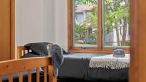 A single bed with a dark mattress and a gray blanket, a wooden headboard, and a window with a view of trees and houses. - Harmony Ridge by AvantStay | Fireplace, Large Deck & Forest Views (Lake Harmony)
