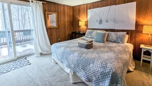 Un dormitorio con una cama grande, una pared de madera, una ventana con cortinas y vistas al exterior.