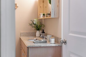 A bathroom with a granite countertop, a white sink, a mirror, a towel, a plant, and a small cabinet.