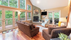 A spacious living room with a fireplace, large windows, and a balcony.