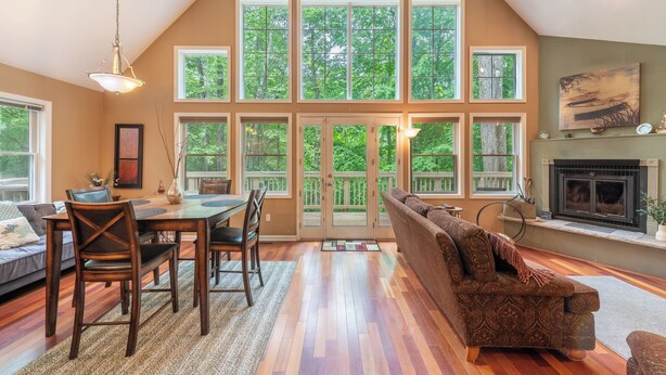 A spacious living room with a high ceiling, a fireplace, and large windows offering a view of the outdoors.