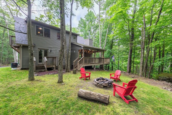 A cabin with a deck, surrounded by trees, and featuring a fire pit and outdoor seating.