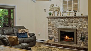 A cozy living room with a stone fireplace, a leather sofa, and a decorative moose head. - Frolic on Fern by AvantStay | Enclosed Deck w/ Forest Views, Bar (Blakeslee)