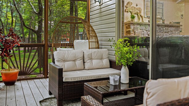 A covered porch with wicker furniture, a glass table, and a potted plant. - Frolic on Fern by AvantStay | Enclosed Deck w/ Forest Views, Bar (Blakeslee)