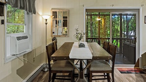 A dining area with a wooden table, chairs, and a view of the outdoors through a glass door. - Frolic on Fern by AvantStay | Enclosed Deck w/ Forest Views, Bar (Blakeslee)