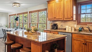 A kitchen with wooden cabinets, a granite countertop, and a large window. - Laker's Pointe by AvantStay | Lakefront Private Peninsula | Hot Tub, Game Room (Long Pond)