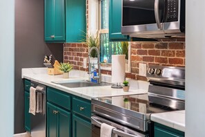 A modern kitchen with teal cabinets, stainless steel appliances, and a brick backsplash.