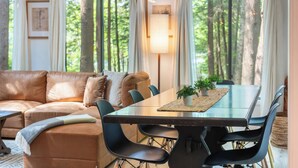 Ein modernes Wohnzimmer mit einem braunen Ledersofa, einem Esstisch mit Glasplatte und schwarzen Stühlen sowie einer Stehlampe.