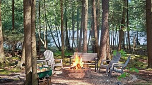 Ein Waldcampingplatz mit Feuerstelle, Stühlen und einer Bank.