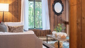 Ein gemütliches Zimmer mit Bett, Tisch mit Blumen, Spiegel und einem fenster mit Vorhängen.