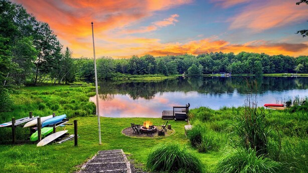 Un espace de camping aménagé au bord du lac, avec un foyer et des chaises, entouré d’une végétation luxuriante et offrant une vue dégagée sur le lac.
