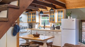 A rustic kitchen with wooden beams, a wooden table with stools, and a refrigerator. - Arrowhead Lake Retreat by AvantStay | Shared Pool, Game Room, Firepit (Pocono Lake)