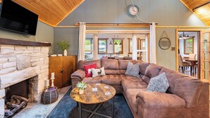 A cozy living room with a stone fireplace, a brown leather sectional sofa, and a wooden ceiling. - Arrowhead Lake Retreat by AvantStay | Shared Pool, Game Room, Firepit (Pocono Lake)