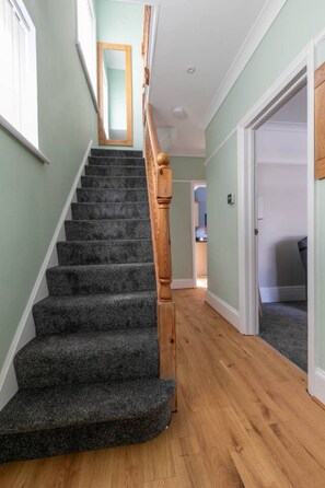 Eine Treppe mit Teppichstufen führt zu einer Zwischenebene, begleitet von hellgrünen Wänden und Holzdielen.