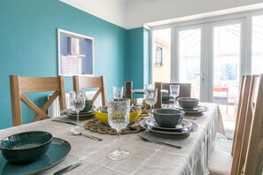 Una mesa de comedor con cristalería, cuencos y platos, con paredes color turquesa y una ventana al fondo.