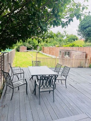 Eine Terrasse mit Tisch und Stühlen, umgeben von einem Holzzaun und viel Grün.