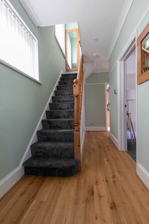 A staircase with dark carpeted steps leading to a landing, flanked by light green walls and wooden flooring.
