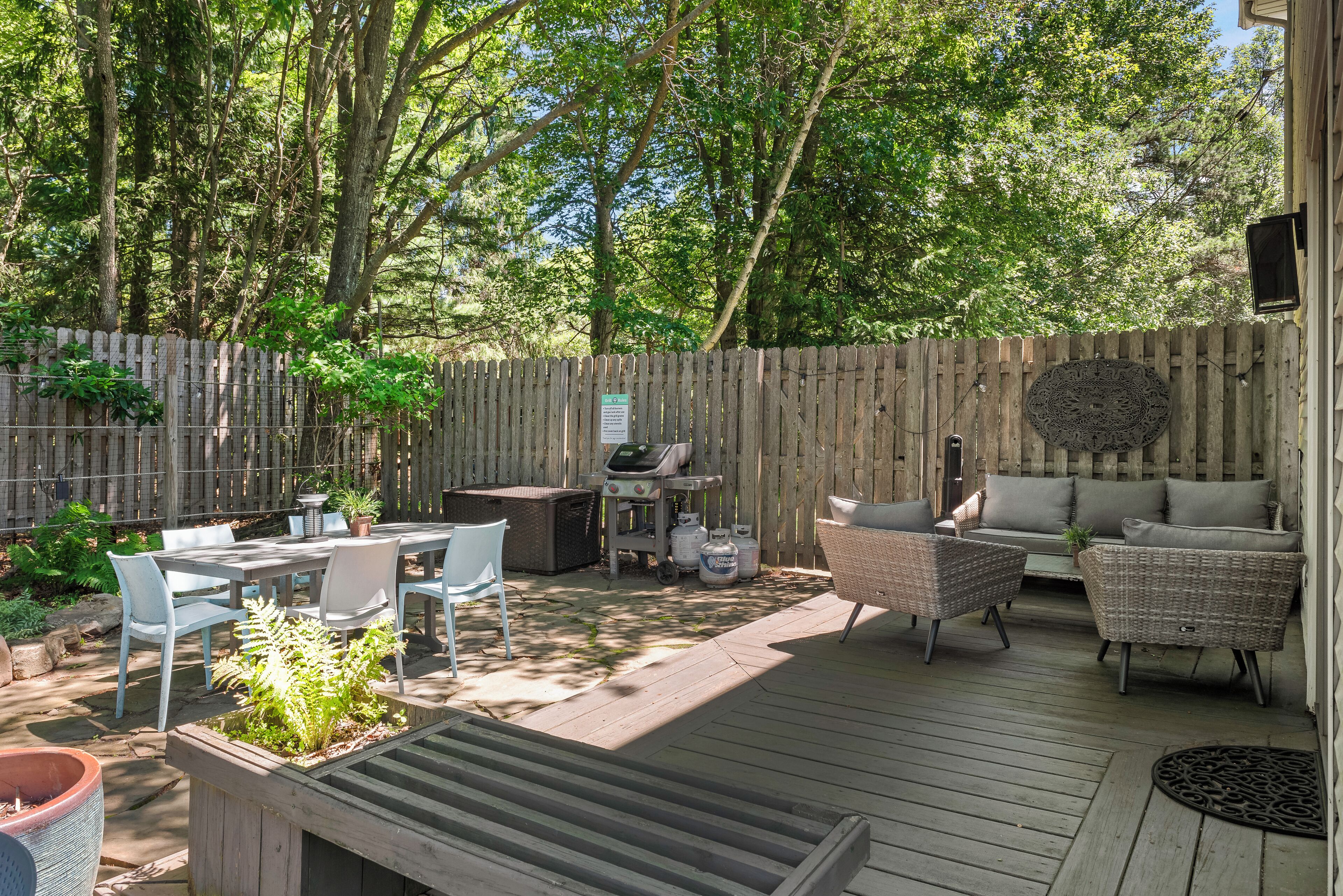 Une terrasse en bois avec des meubles d’extérieur, un barbecue et un espace clos agrémenté d’arbres.