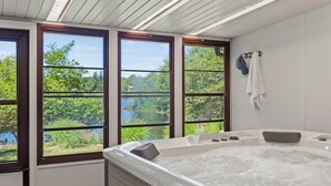 A spa room with a hot tub, large windows, and towels on hooks. - Simply Shores by AvantStay | Private Beach + Dock | Lake Overlook (Long Pond)