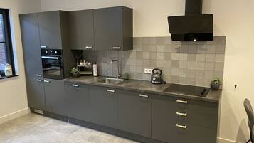 Een moderne keuken met donkere kastjes, een inbouwoven, een waterkoker en een spoelbak.