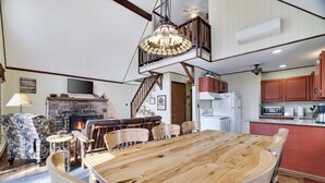Un vaste salon doté d’une grande table à manger en bois, de sièges confortables, d’une cheminée et d’un escalier menant à un niveau supérieur.