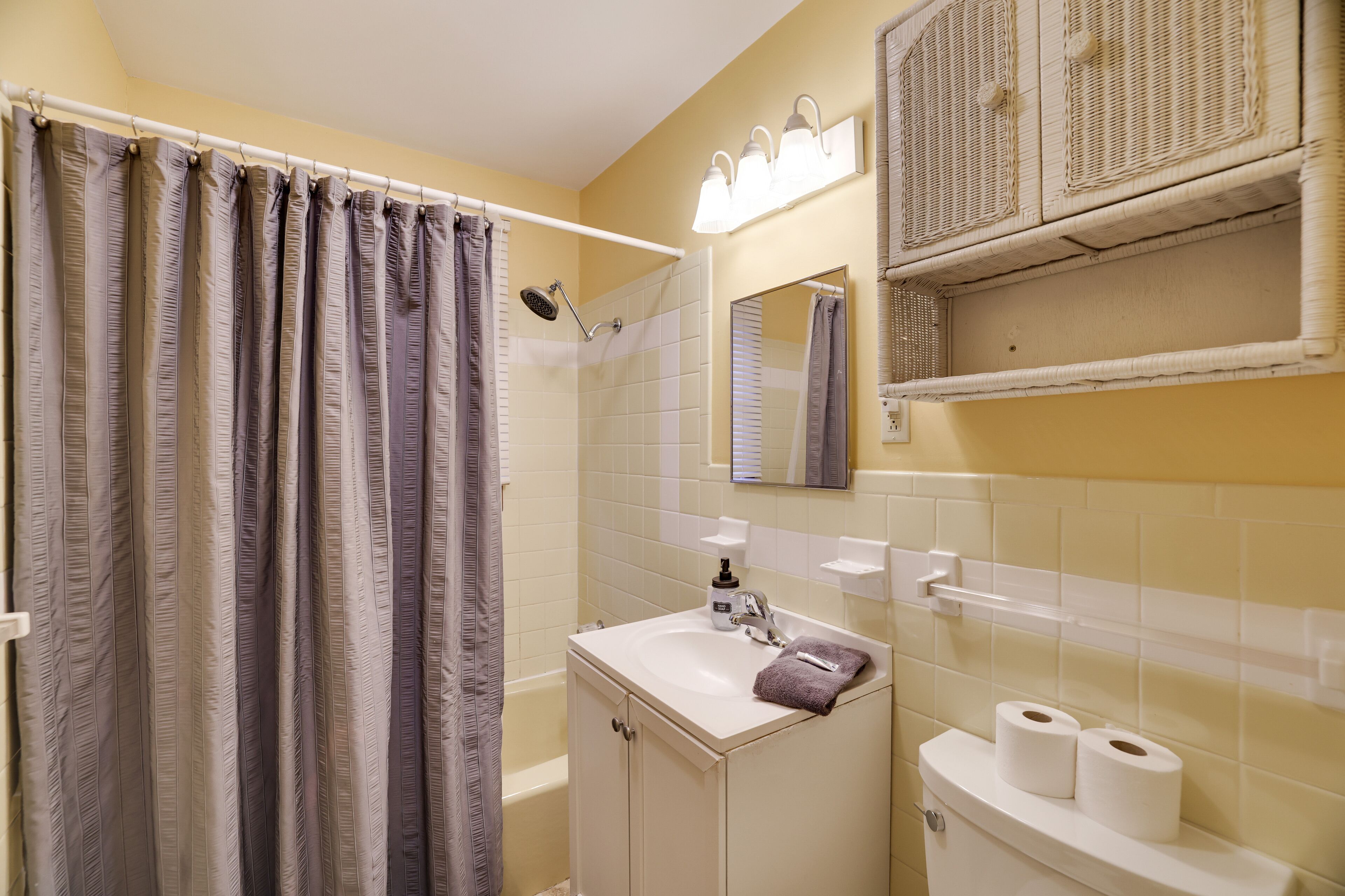 A bathroom with a shower curtain, a sink with a towel, a mirror, and a toilet with toilet paper.
