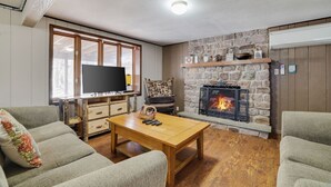 Un salon avec une cheminée en pierre, des meubles en bois et un téléviseur posé sur un meuble.