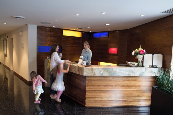 Zona de recepción con mostrador de madera, pantalla digital y planta en maceta.