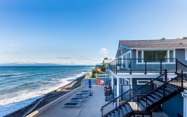 A coastal building with a balcony overlooking the sea, a staircase, and a paved walkway with sun loungers. - Qualicum Beach Ocean Suites  (Qualicum Beach)
