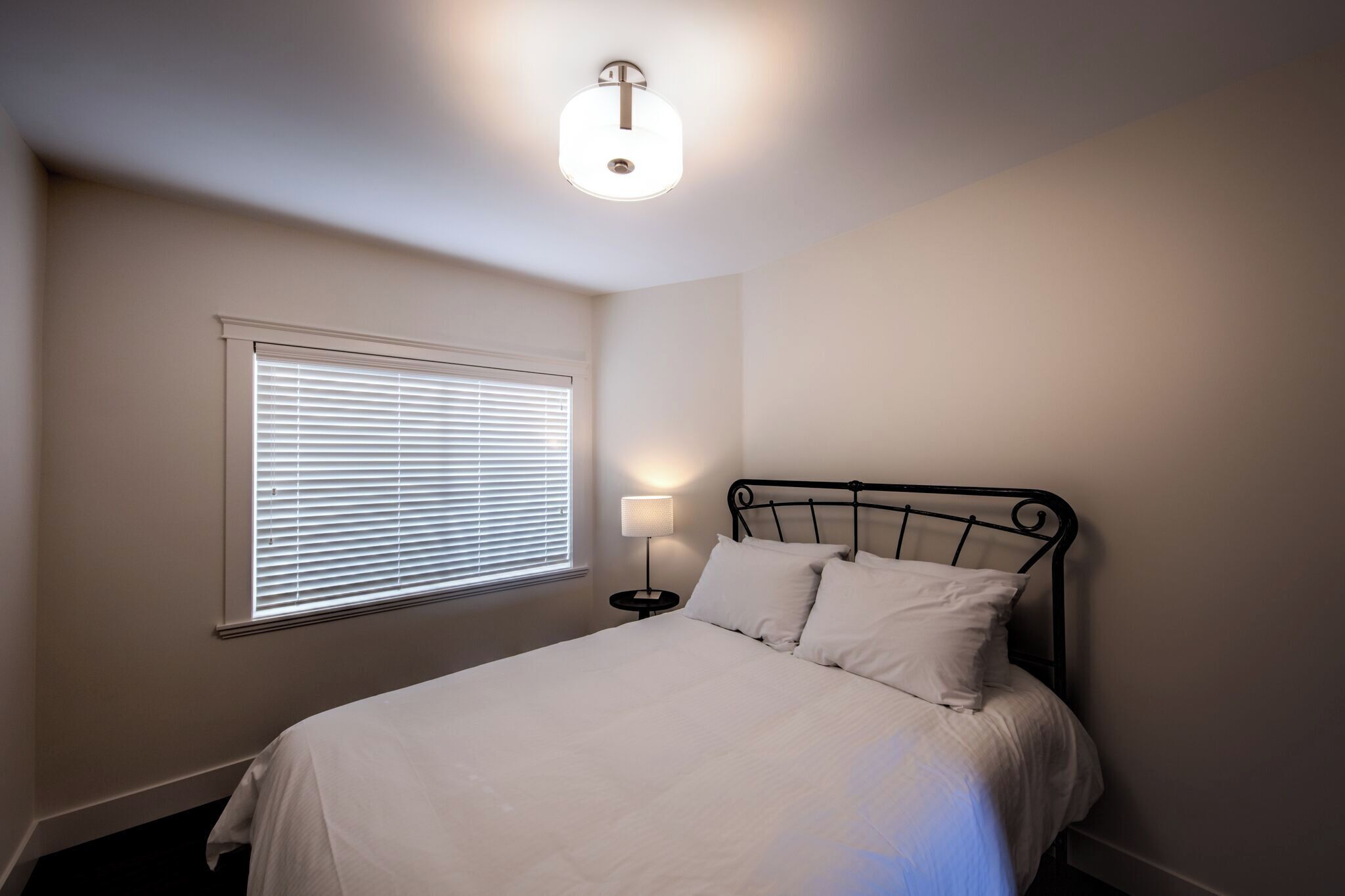 A bedroom with a bed, a bedside table, a lamp, and a window with blinds.