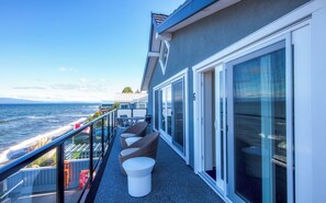 A balcony with a view of the ocean, furnished with wicker chairs and a white table. - Qualicum Beach Ocean Suites  (Qualicum Beach)