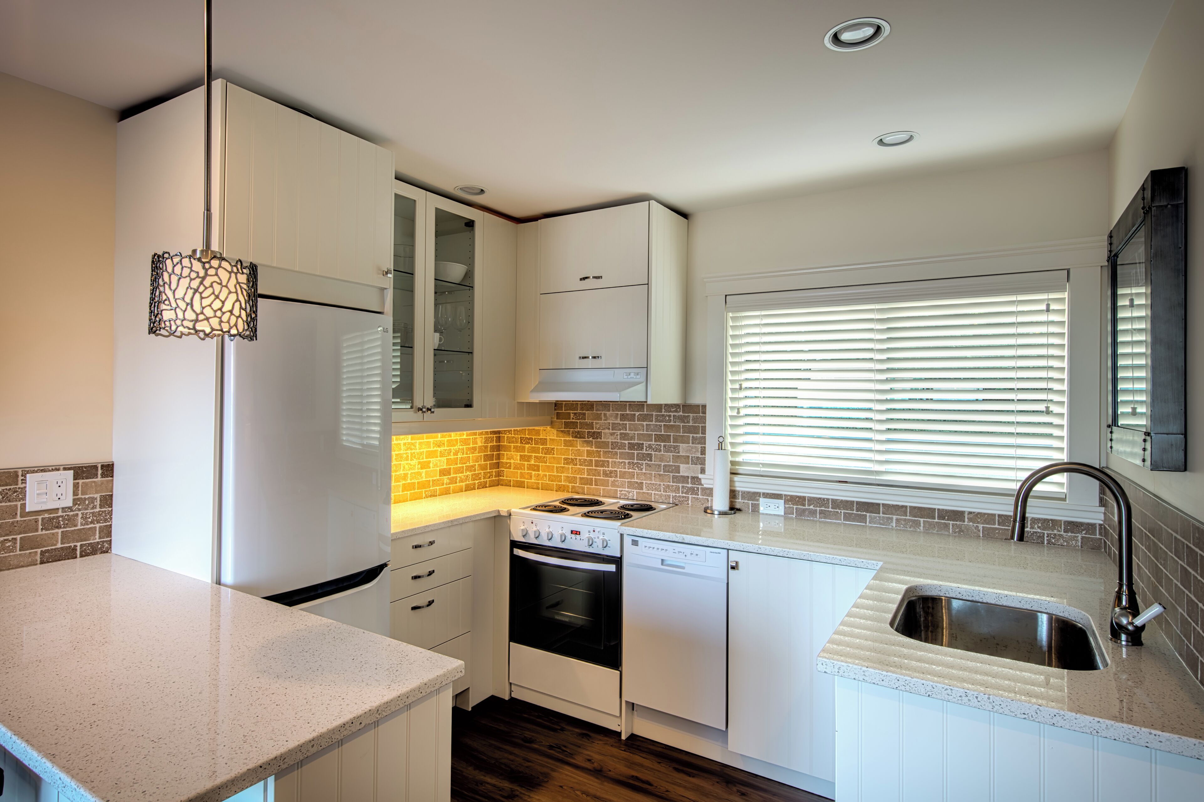 A modern kitchen with white cabinetry, a built-in oven, a dishwasher, and a stainless steel sink.
